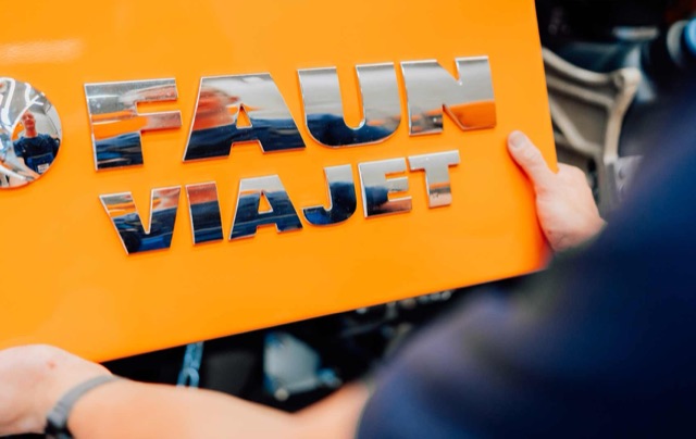 Hand hält ein orangefarbenes Schild mit dem Schriftzug FAUN Viajet