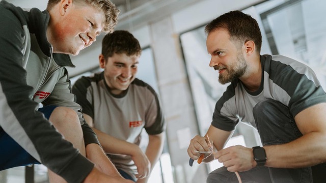 Zwei Azubis und ein erfahrener Elektriker der FEST GmbH lachen über den Bauplänen