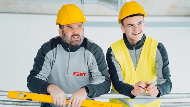 Zwei Elektriker mit Helm lehnen auf der Baustelle am Geländer