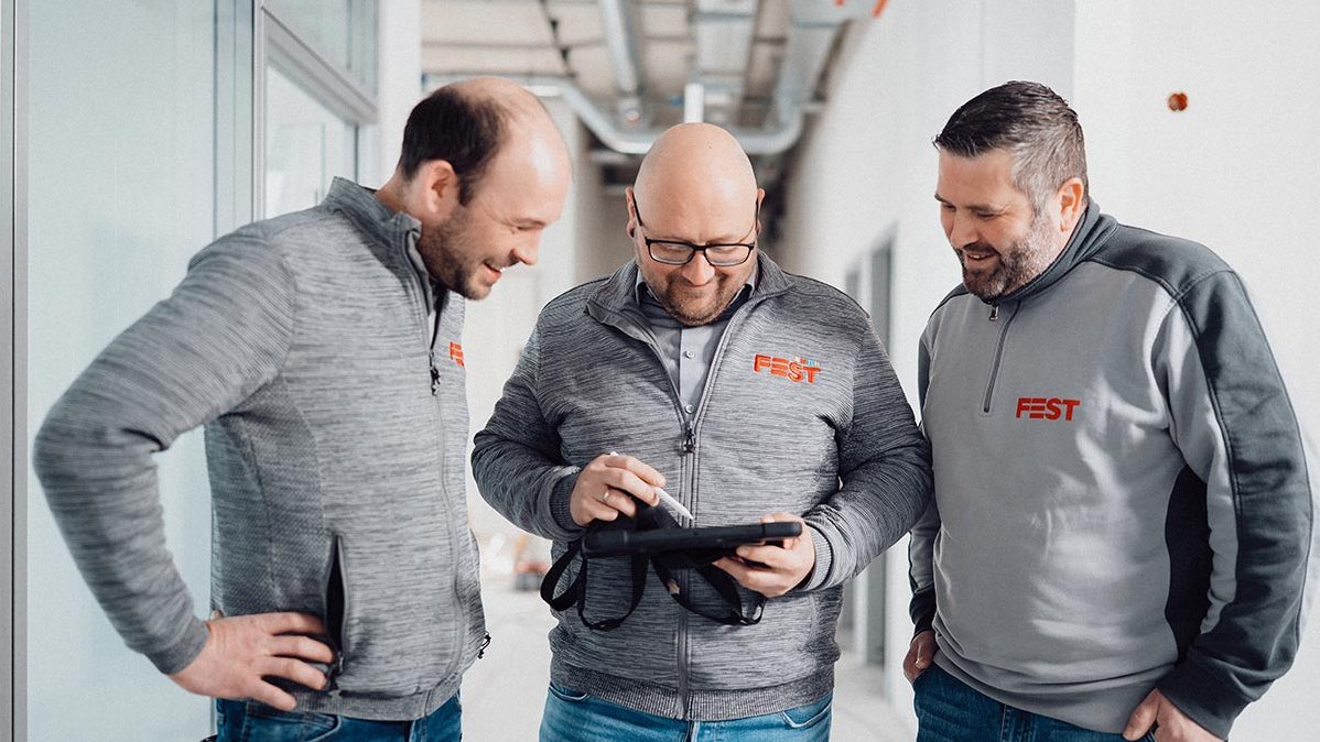 Drei Mitarbeiter der FEST GmbH besprechen ein Projekt am Tablet