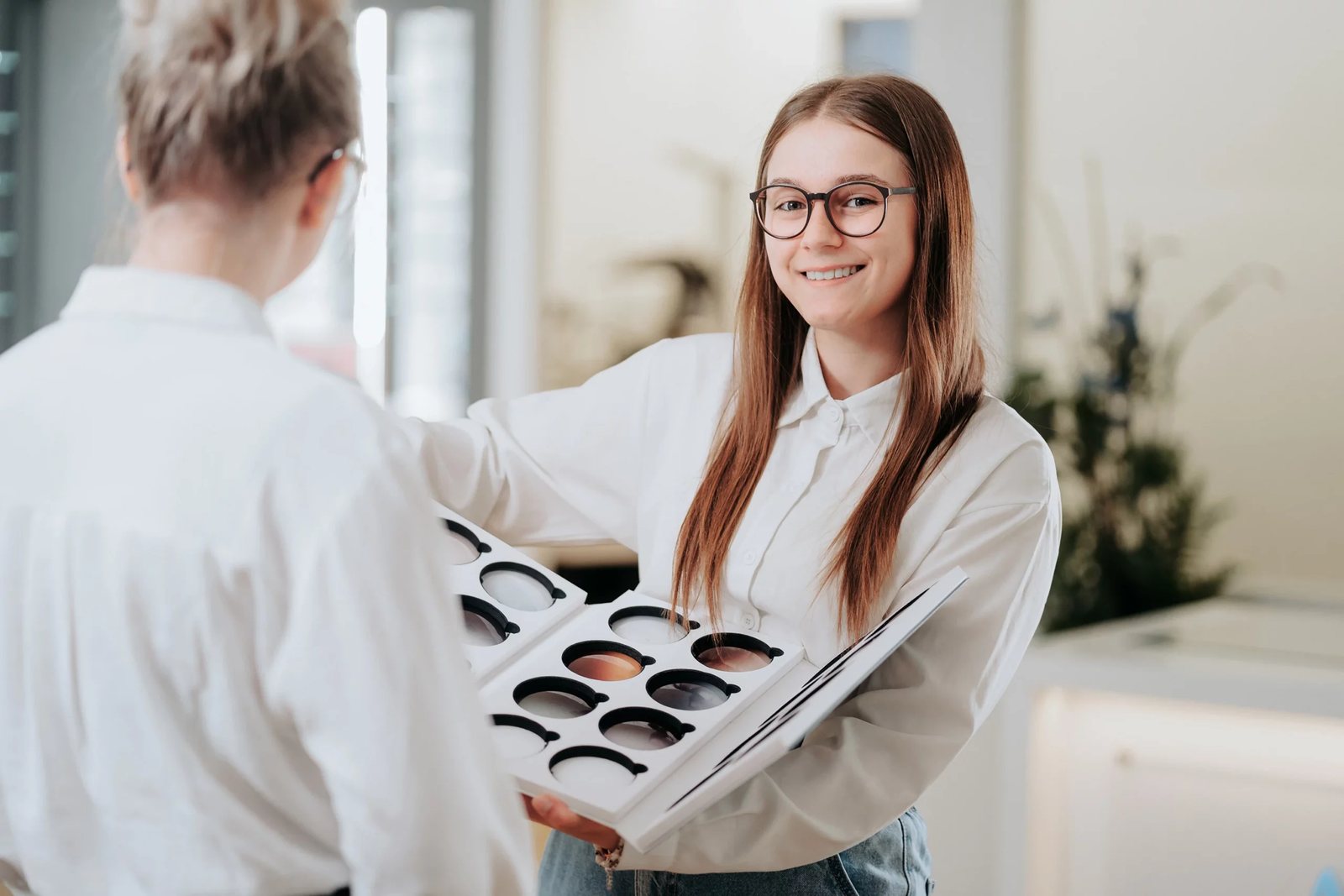Mitarbeiterin zeigt einer Kundin eine Mustertafel mit getönten Brillengläsern