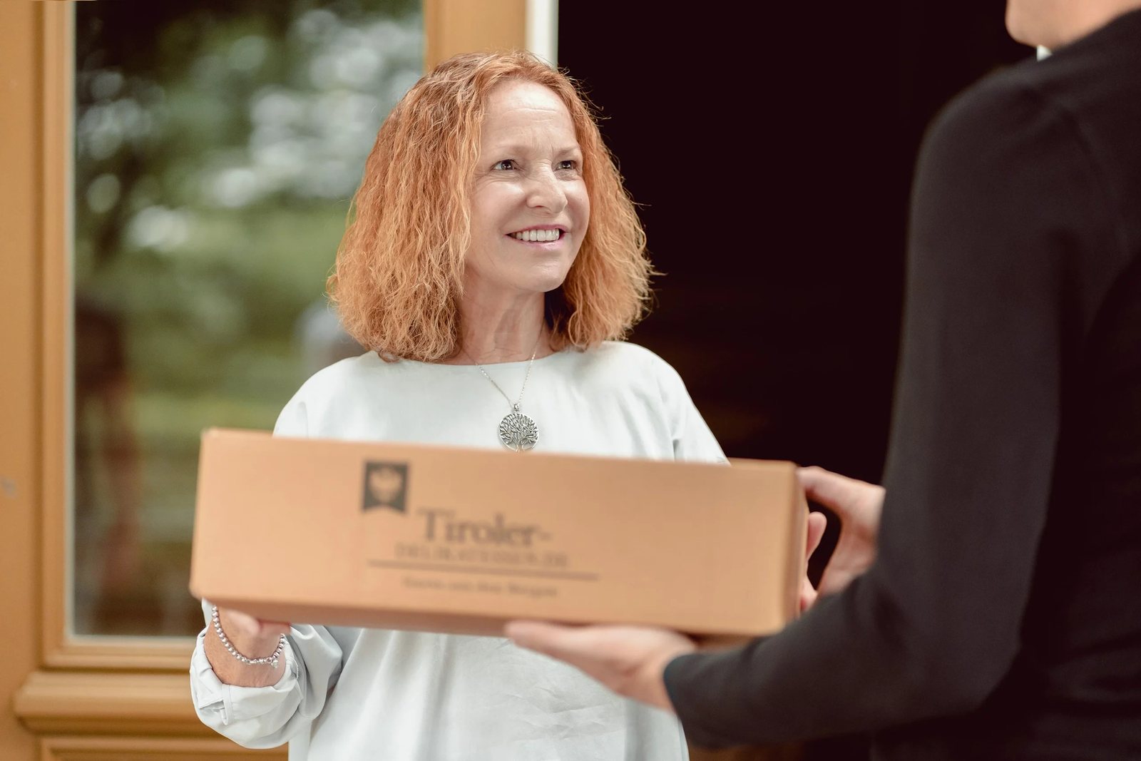 Frau nimmt an der Haustür ein Paket von Tiroler Delikatessen entgegen