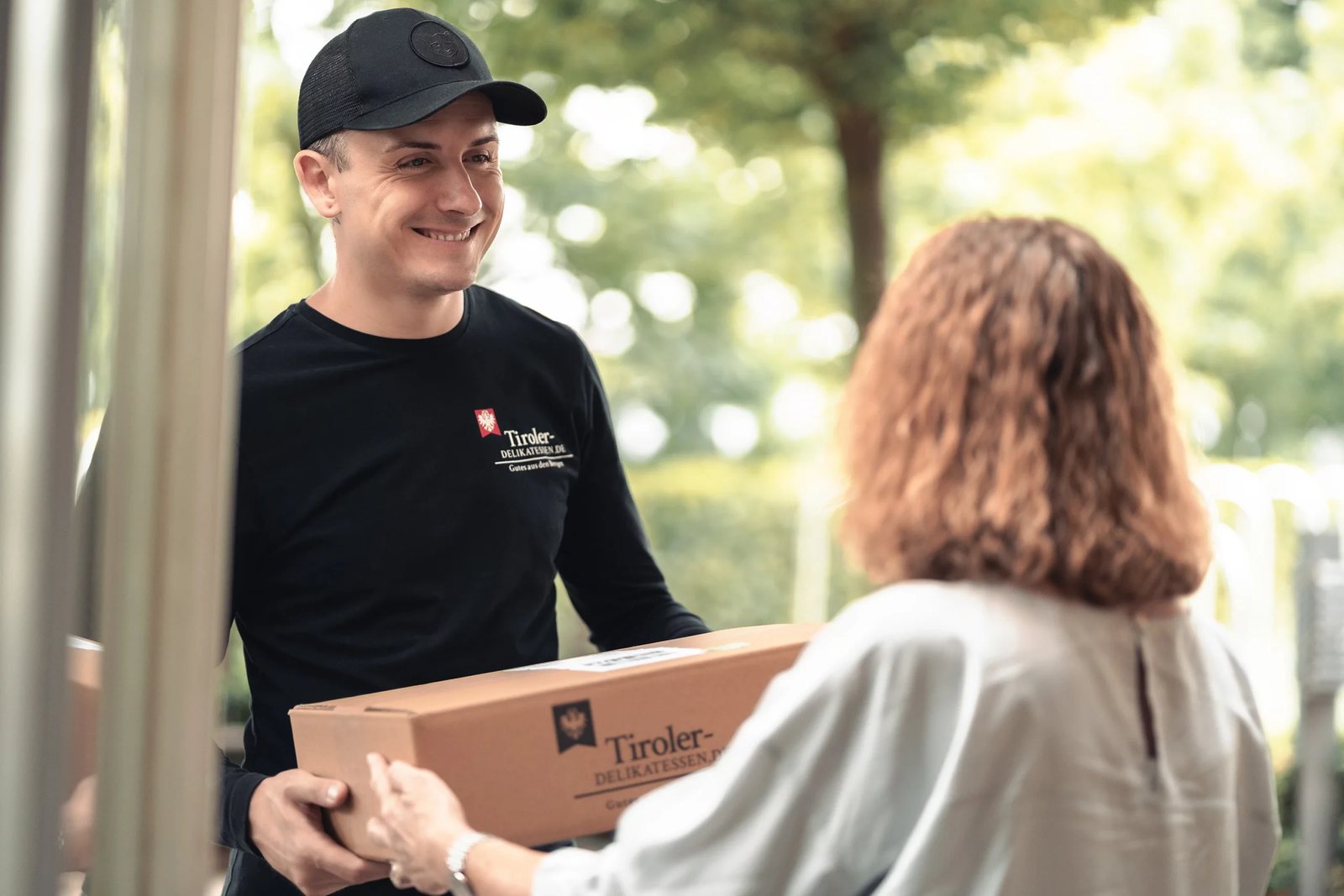 Mitarbeiter von Tiroler Delikatessen übergibt ein Paket an eine Kundin